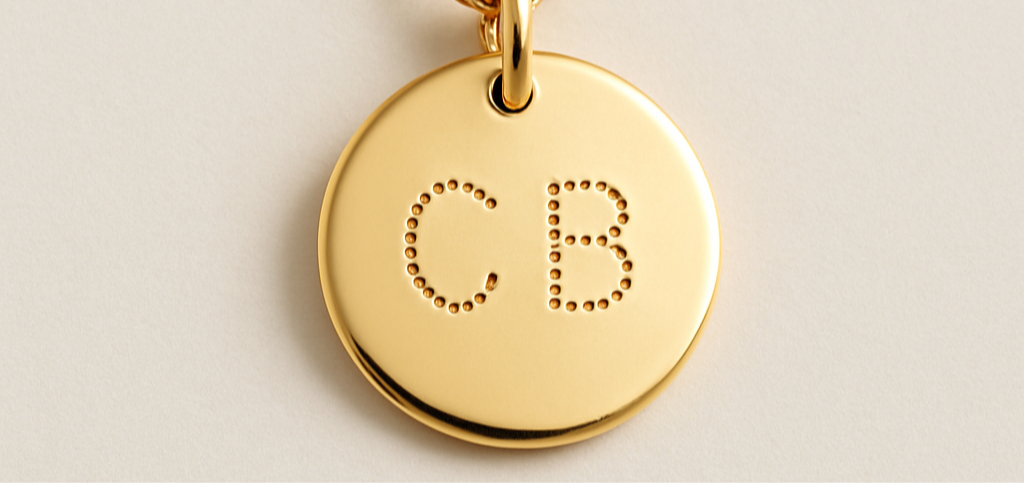 Gold necklace with a round pendant engraved with 'CB' on a light background