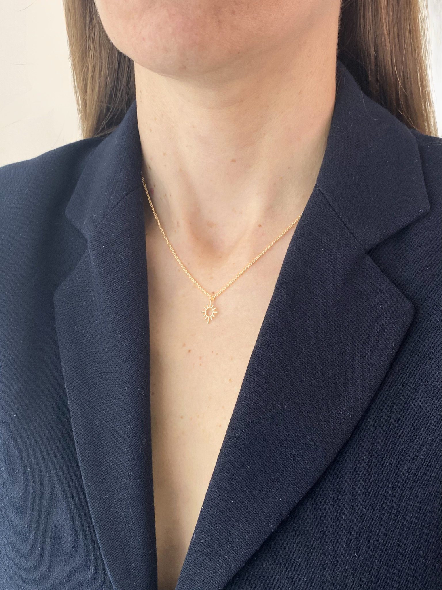 Person wearing a sun gold necklace with a navy blazer