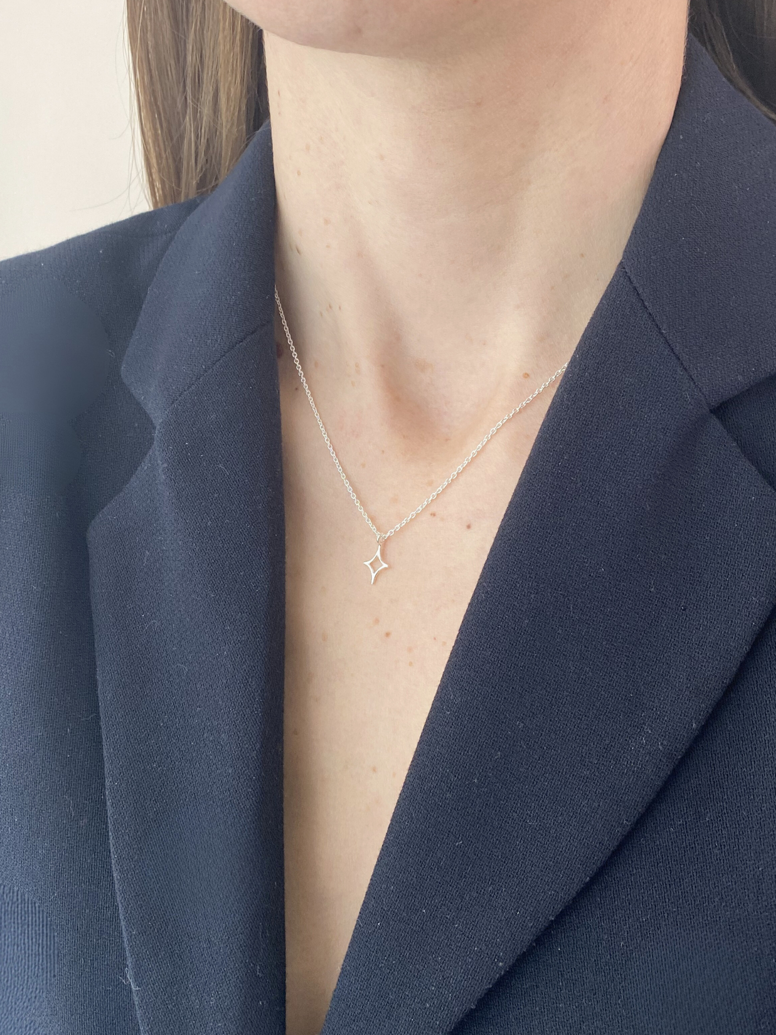 Person wearing a delicate star necklace with a blue blazer